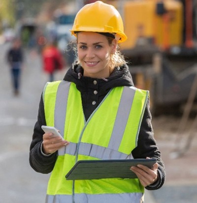 Woman in a high-vis vest and yellow hard hat holding an electronic device and mobile phone